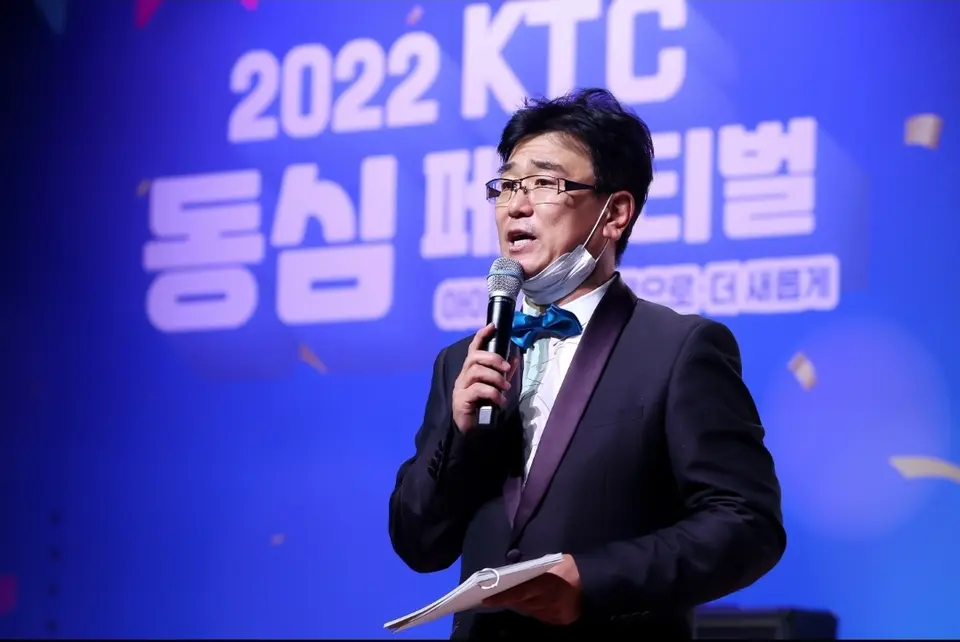 파란 무대 배경 앞에서 마이크를 들고 진행하는 MC 신용주